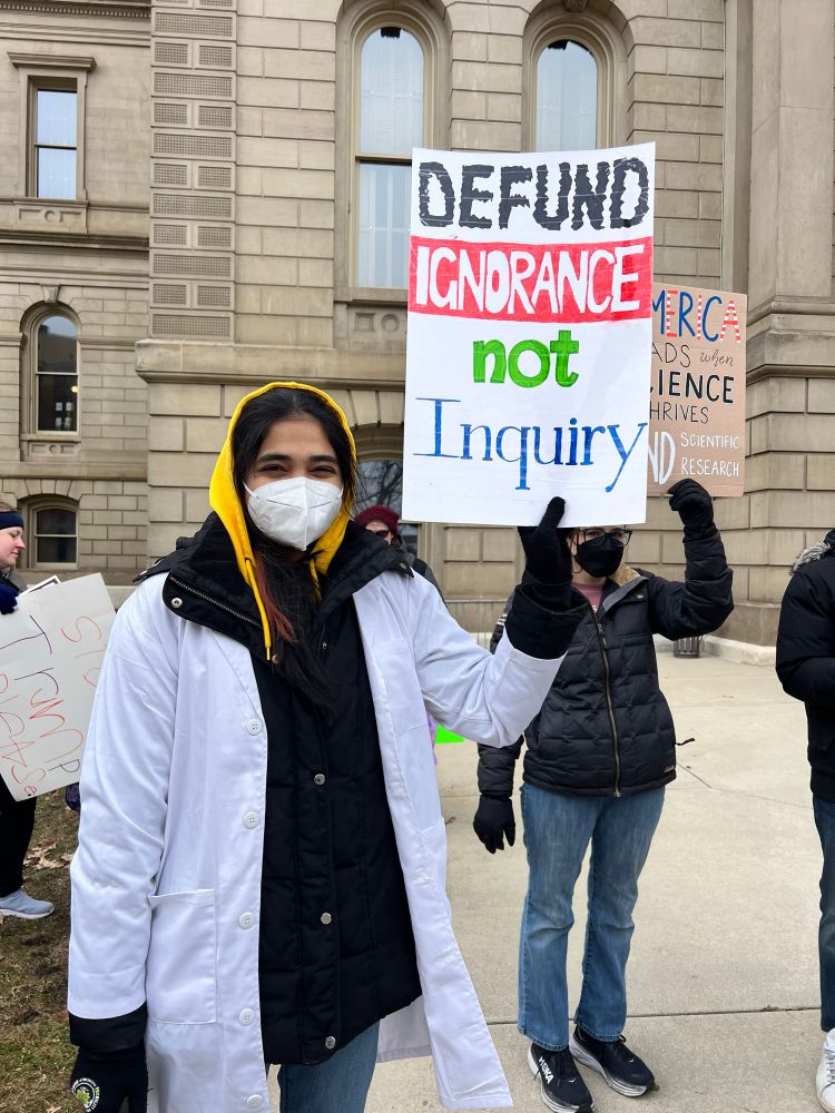 Woman holding a sign: Defund Ignorance not Inquiry