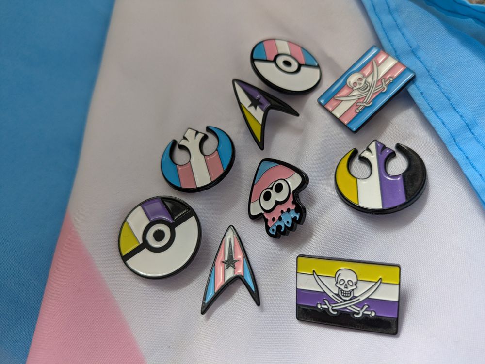 Star wars, star trek, Pokémon, pirate and Splatoon trans and non-binary flag pins on a trans flag