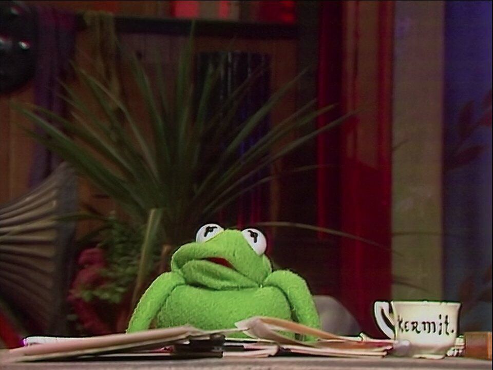 Kermit the frog sat at a desk looking overwhelmed and with his neck completely absent