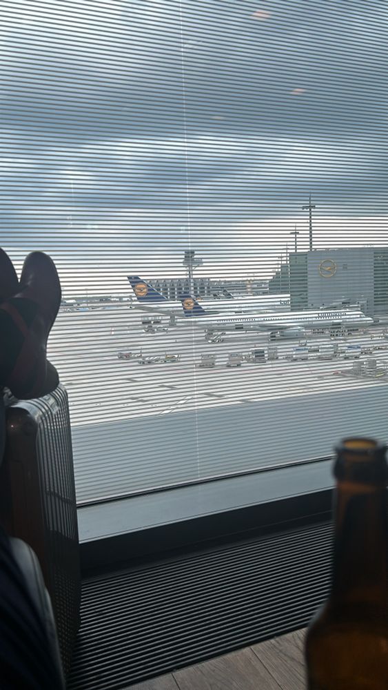 Am Flughafen. Im Hintergrund die wartenden Flugzeuge. Entspannte Füße links, ein Bier rechts