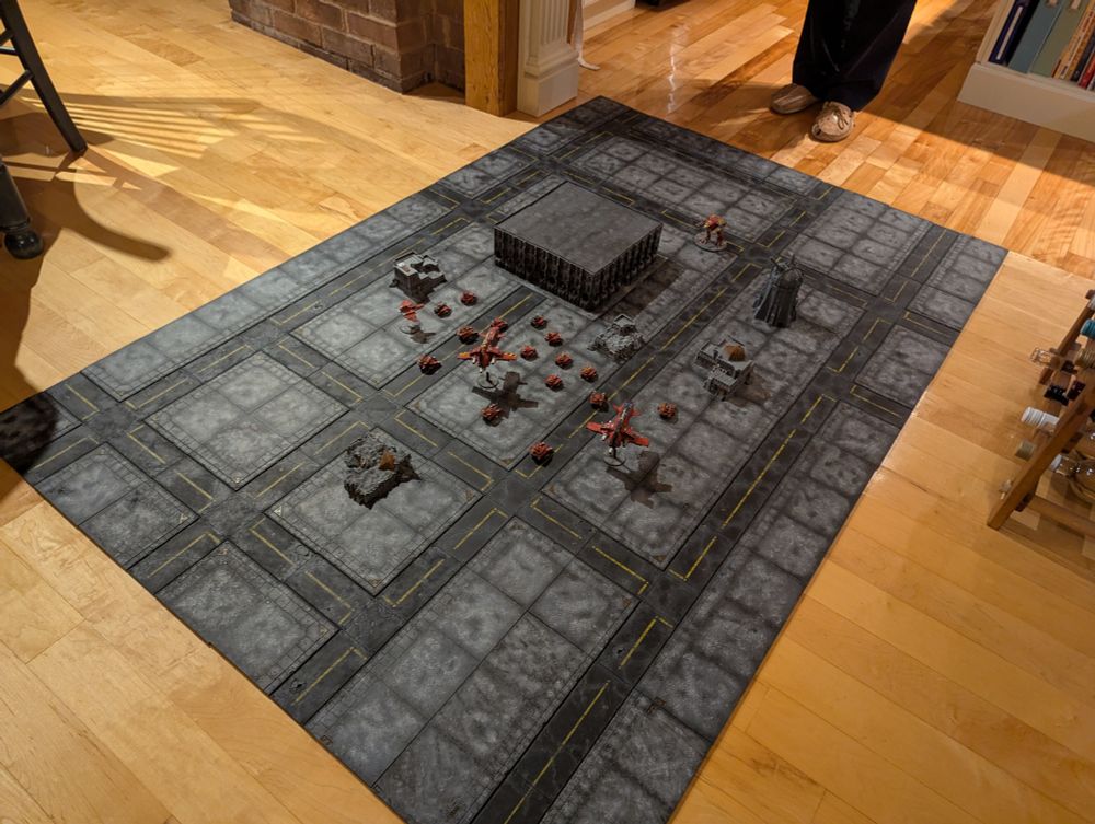 A full 6'x4' set of Legions Imperialis scale road tiles fully painted in a grey and black scheme complete with road markings, along with an assortment of Blood Angels vehicles and aircraft, buildings both ruined and whole and a Legions Imperialis scale Warhound Titan to show scale. This picture also includes a large structure in the middle.