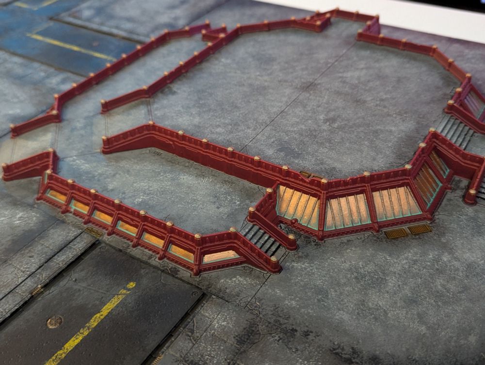 A pair of elevated plaza tiles sit with other city tiles for the game Legions Imperialis. This plaza has red and copper cladding. Shot is taken from close to the side.