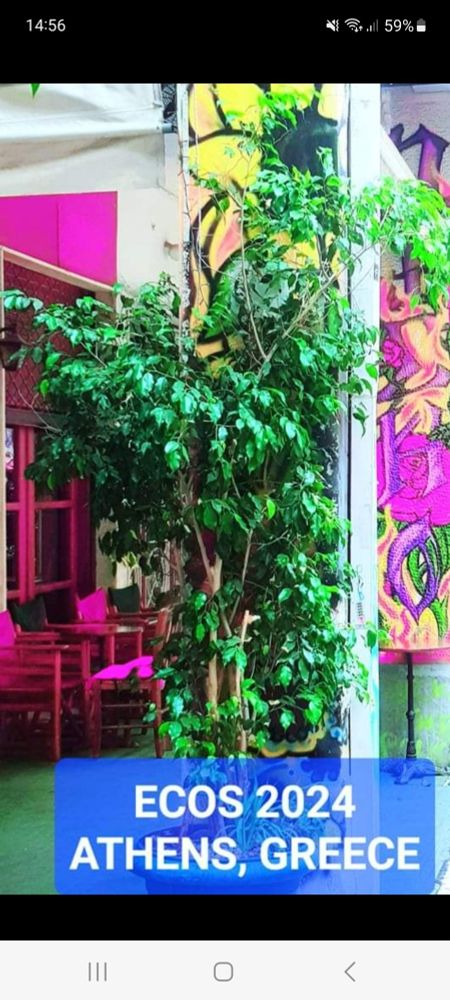 A green tree in a big pot stands in front of pink chairs and tables. In the background a huge picture with pink and yellow flowers. Text: Ecos2024 Athens, Greece