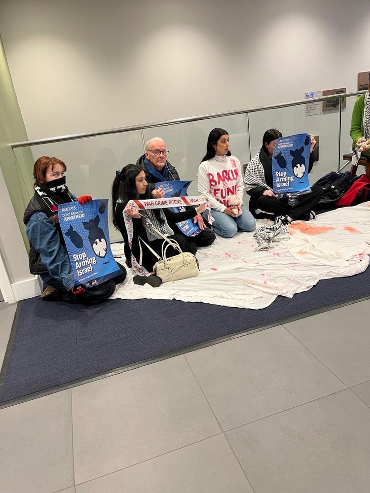 Six activists sit around a “blood soaked “ sheet as they occupy Barclays Bank
