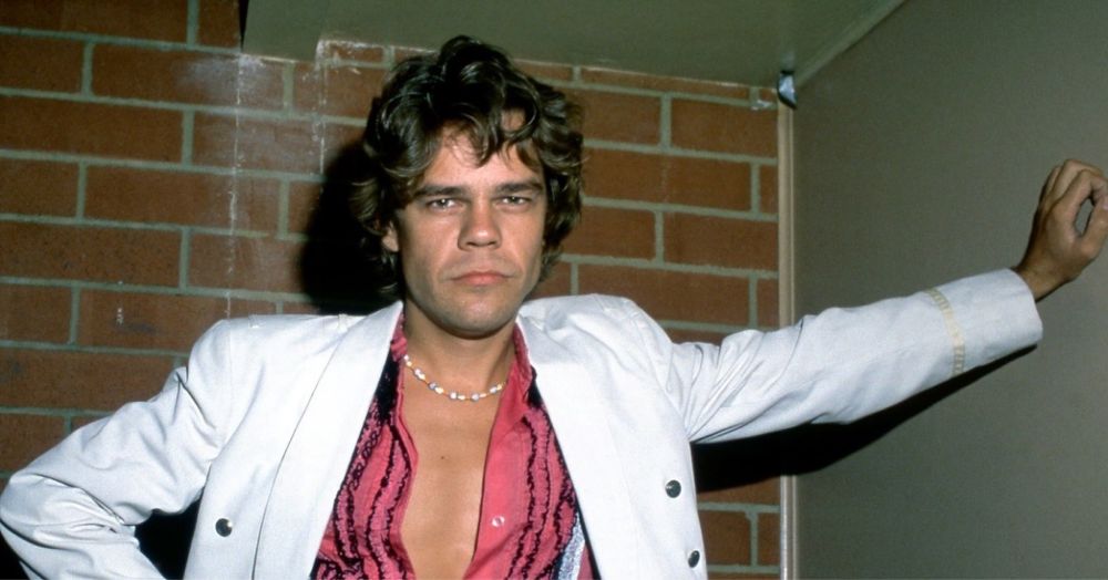 David Johansen in a white coat posing with one hand on a wall