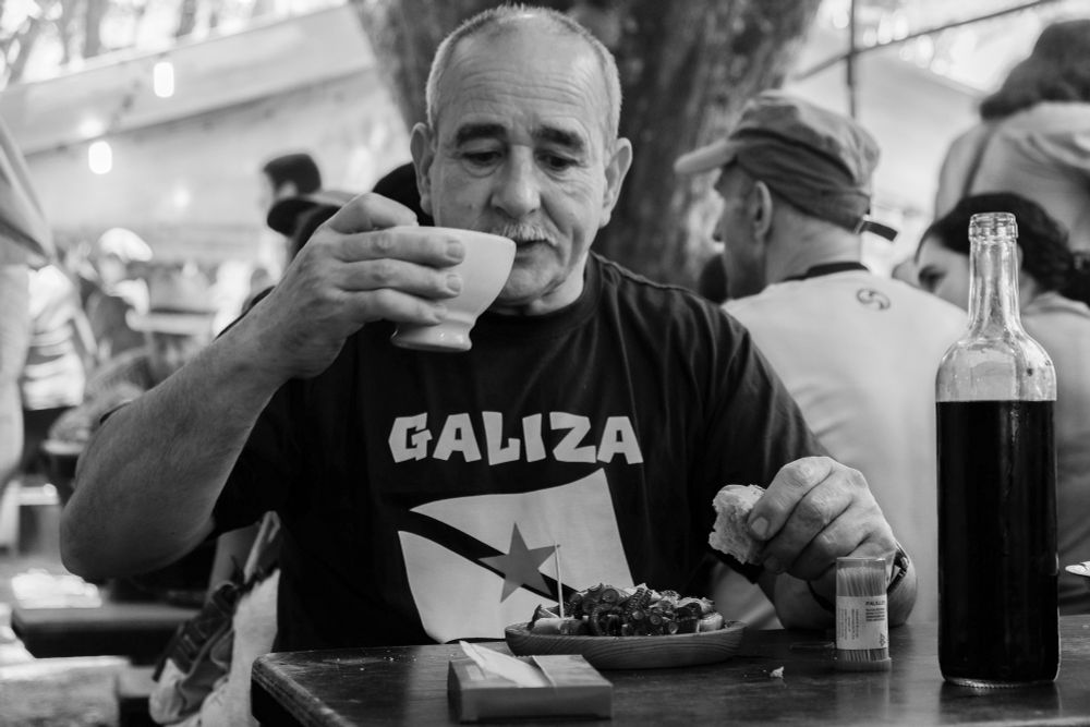 Un home bebendo viño e comendo polbo á feira.