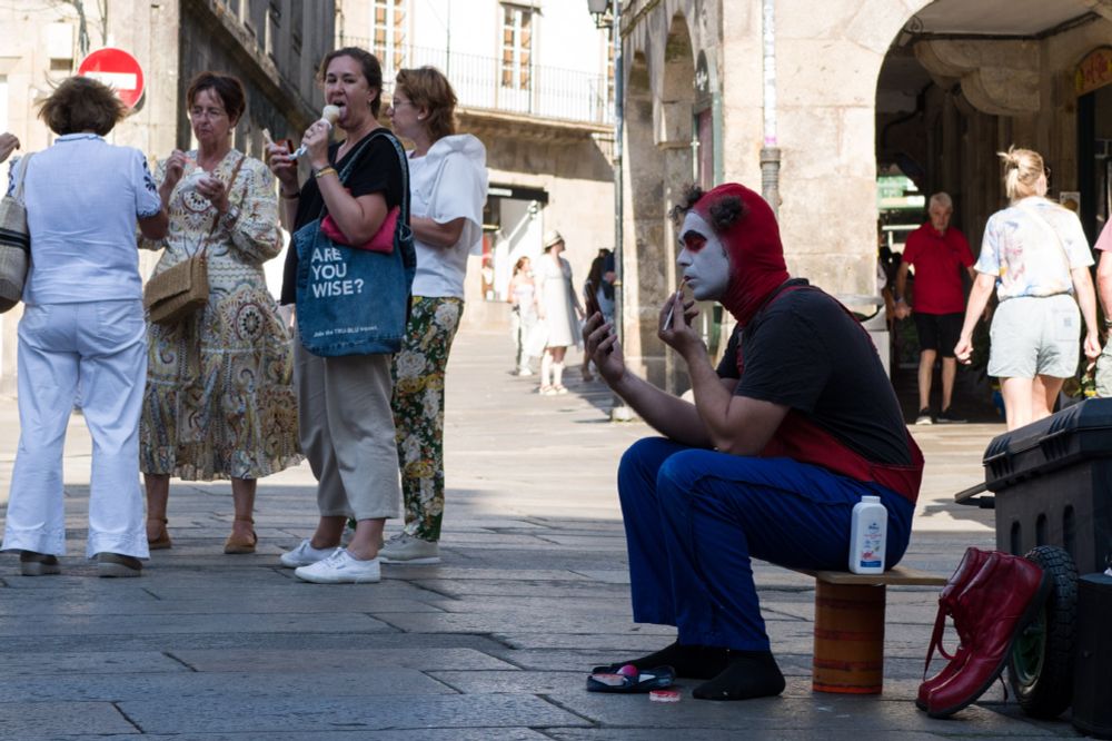 Un clown pintándose los labios, mirado por una señora que come un helado.