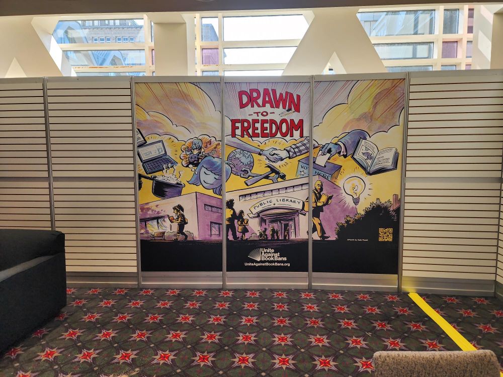 The Unite Against Book Bans booth in the ALA Connect Lounge at ALA Annual Conference 2025, featuring panels with #DrawnToFreedom artwork by Nate Powell.
