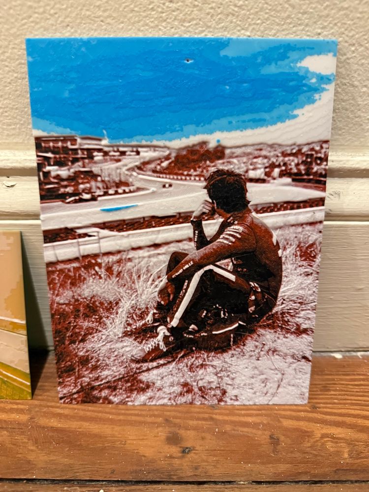 A hueforge 3d print of F1 driver Charles Leclare overlooking the hills of a track.