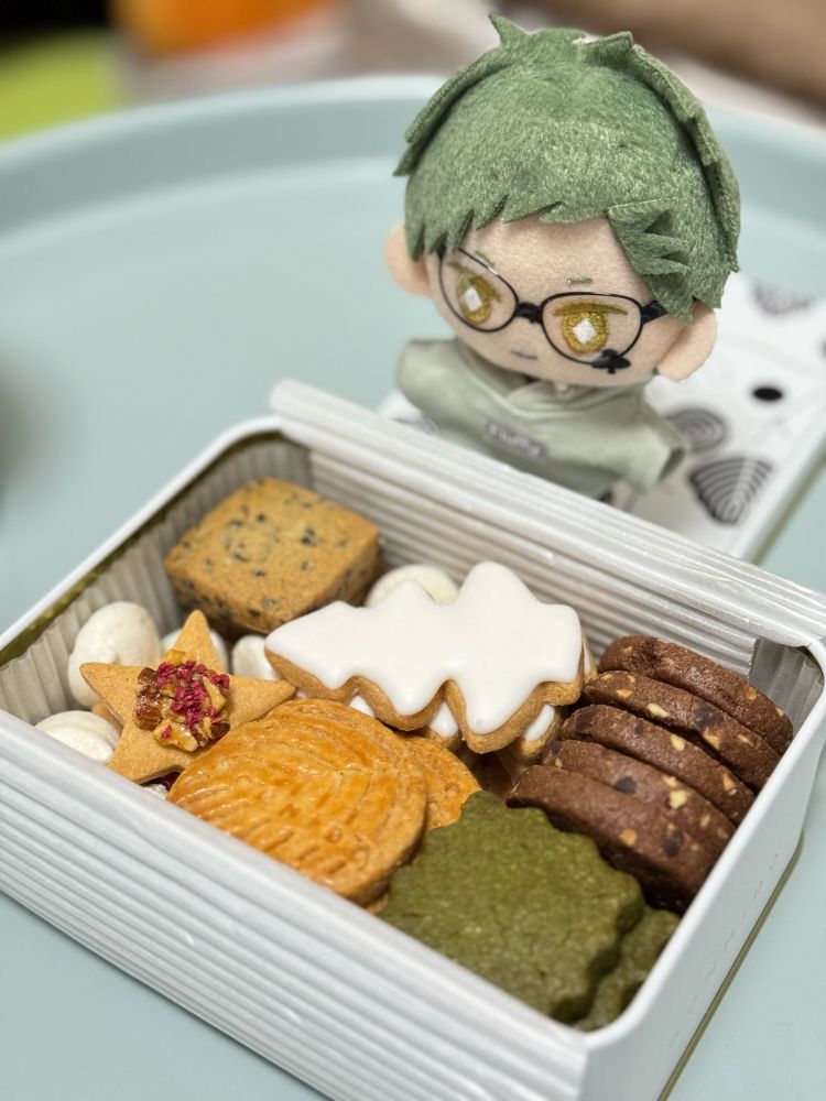 商品名「HONMIDOクッキー缶 冬」。抹茶やチョコやアイシングクッキーなど、6種類のクッキーが缶に詰まっていてとても美味しい。右上ではトレぬいが缶の中身を眺めて、俺が作りました、の顔をしている。