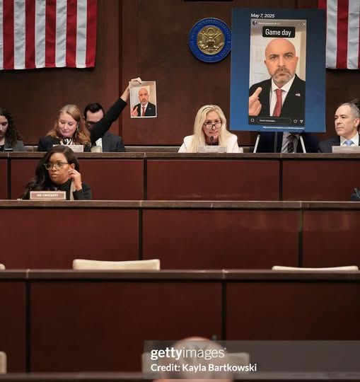 A picture of the dais of the DOGE subcommittee, chaired by Marjorie Taylor Greene, who sits in front of a photo of a man holding two fingers in a peace sign, with one finger cropped out of the frame to make it seem as if he's giving the camera (and the committee) the middle finger.
To Greene's left, Rep. Melanie Stansbury holds high a copy of the original photo.