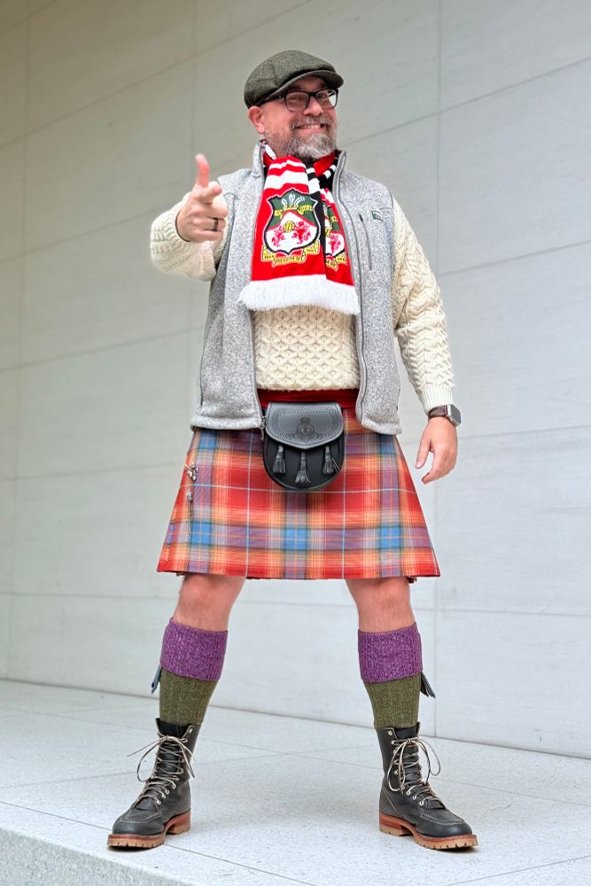 Photograph of a middle aged, white man, wearing a Grand Canyon tartan kilt, black sporran, cream Aran sweater, grey vest, flat cap, and WREXHAM AFC SCARF!

He stands with his lovely legs akimbo, fantastic boots planted, and a finger gun cocked and pointed at the camera. A grin graces his face and he challenges you to say ANYTHING about his team today. 