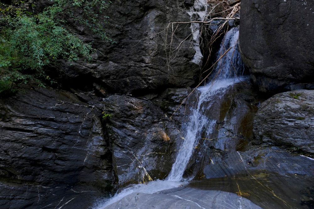 View of a waterfall springing from between some large rocks.