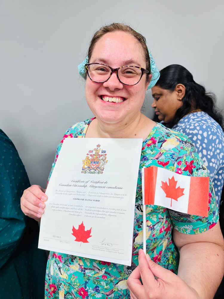 Middle aged white woman with glasses holding a certificate and Canadian Flag.