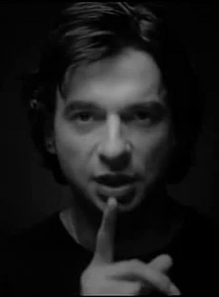 a black and white photo of a man holding his finger to his lips .