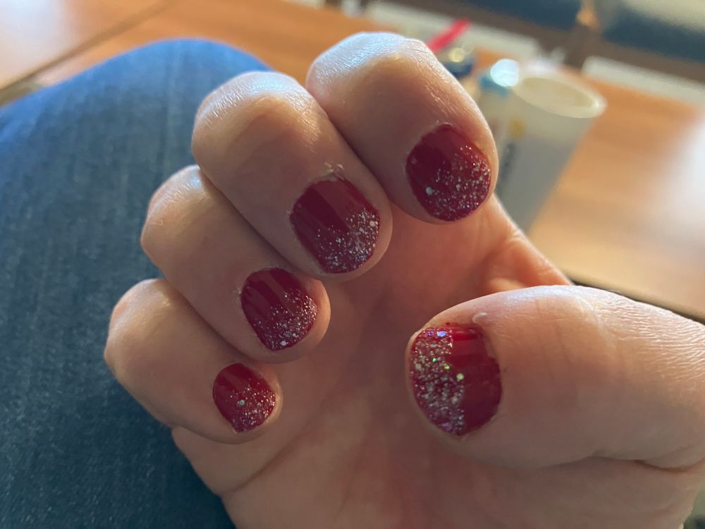 My right hand showing a red polish with glitter ombré effect 