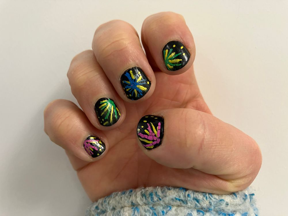 My right hand showing the nails. The nails have a black base and then firework designs with gold, green, pink abc blue starbursts over the top
