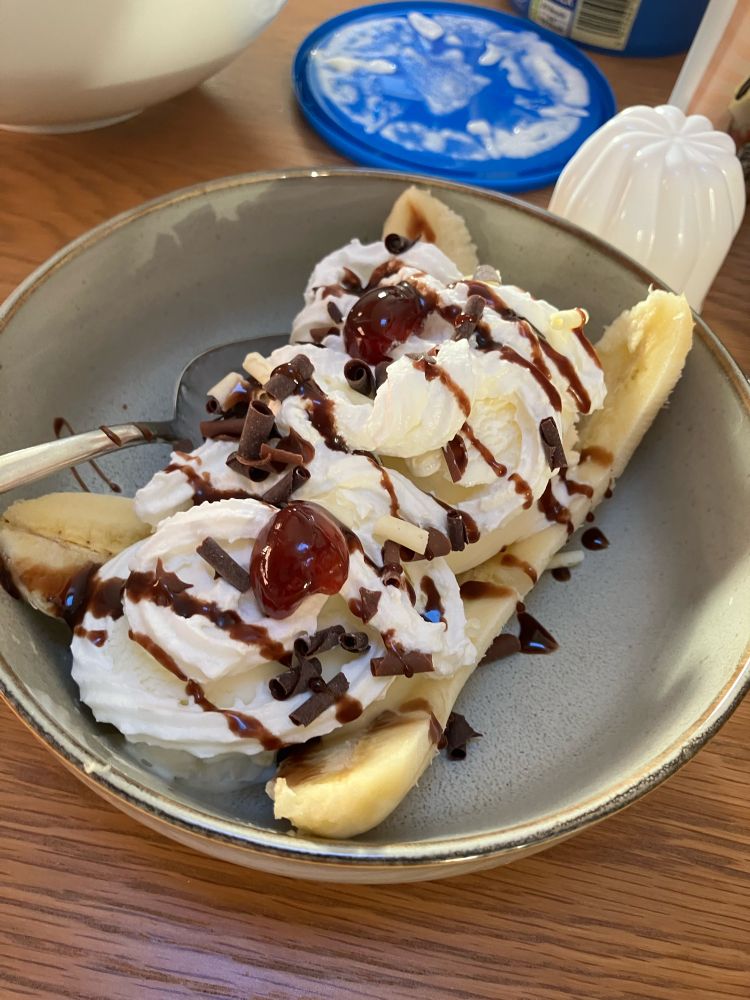 A banana split open in a bowl with ice cream, squirty cream, chocolate sprinkles, chocolate sauce, and glqce cherry