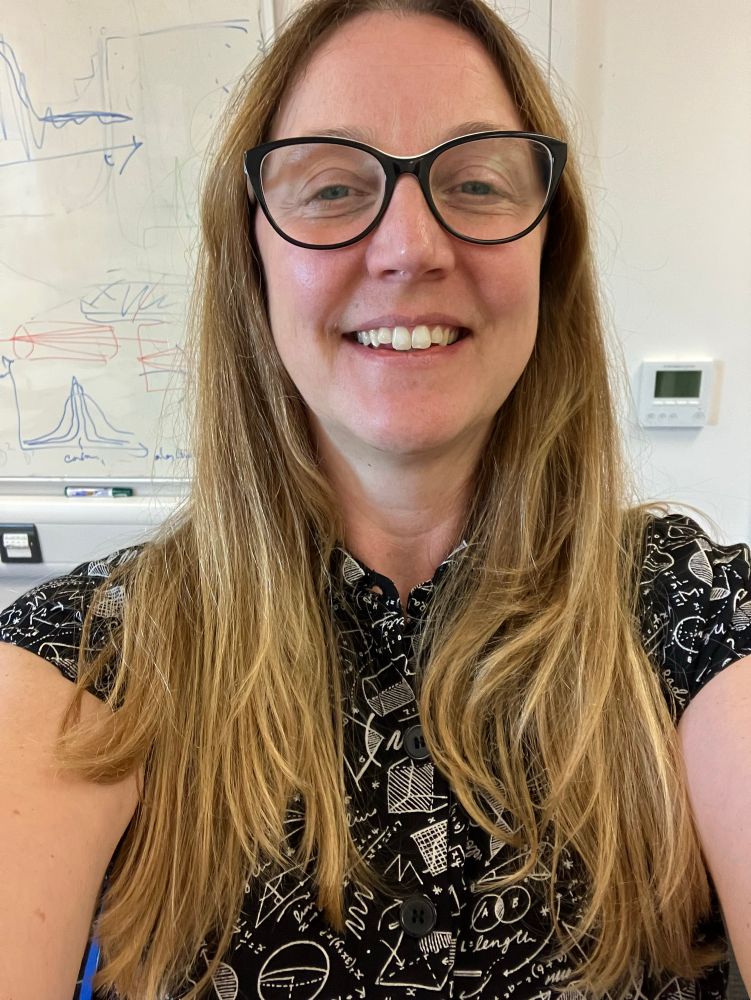 My top half in a black dress with white maths equations abs shapes on it. My hair is down and I have black rimmed glasses on. I look suspiciously happy for the beginning of the semester 