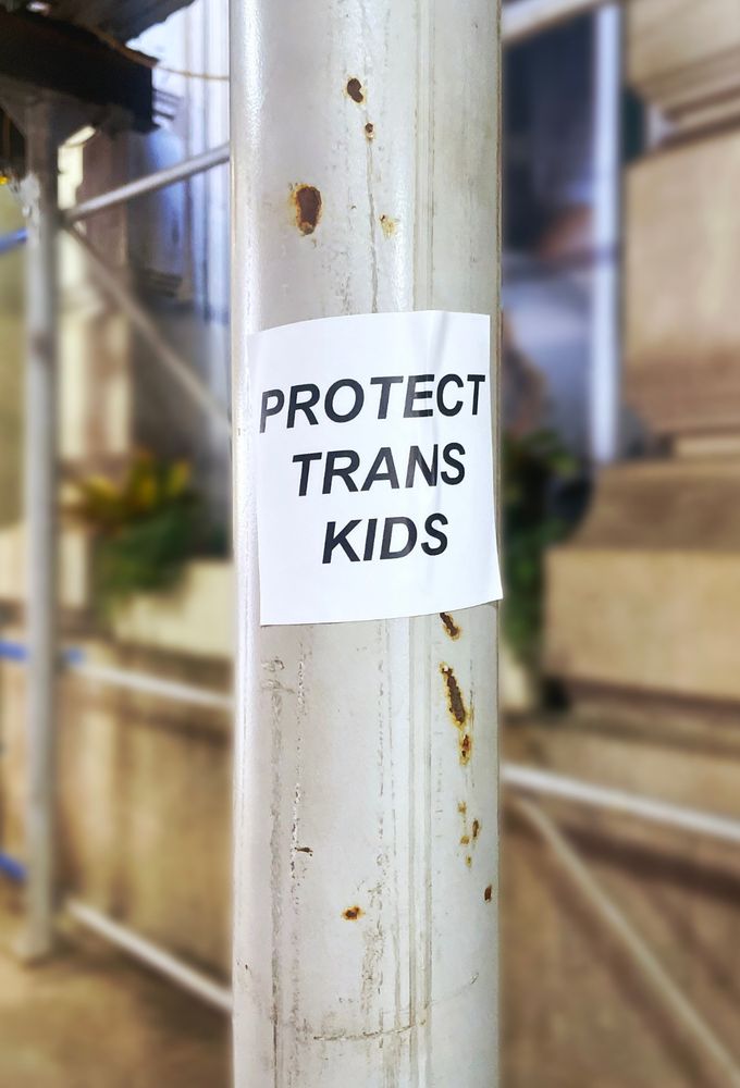 a photo of a city scaffolding and on the pole in focus is a sticker that says "protect trans kids"