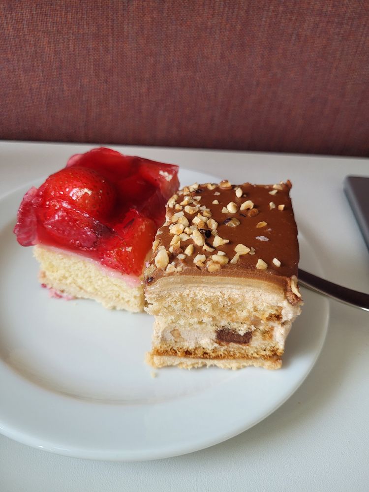 Ein Kuchenteller mit zwei halben Stückchen Torte - links Erdbeertorte, rechts Nougattorte - und einer Kuchengabel 