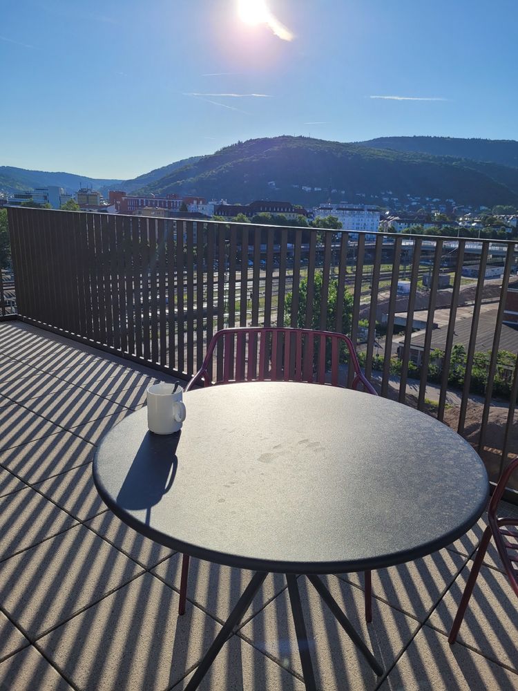 Tasse Kaffee auf einem Tisch der Dachterrasse. Blick auf Berg und Stadt. 