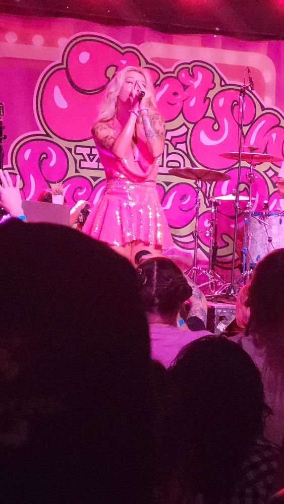 Scene Queen singing into the mic, wearing a pink glittery dress with pink lighting