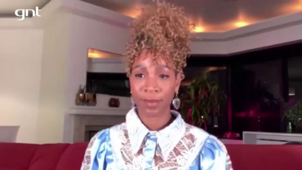 a woman with curly hair is sitting on a red couch in a living room looking at the camera .