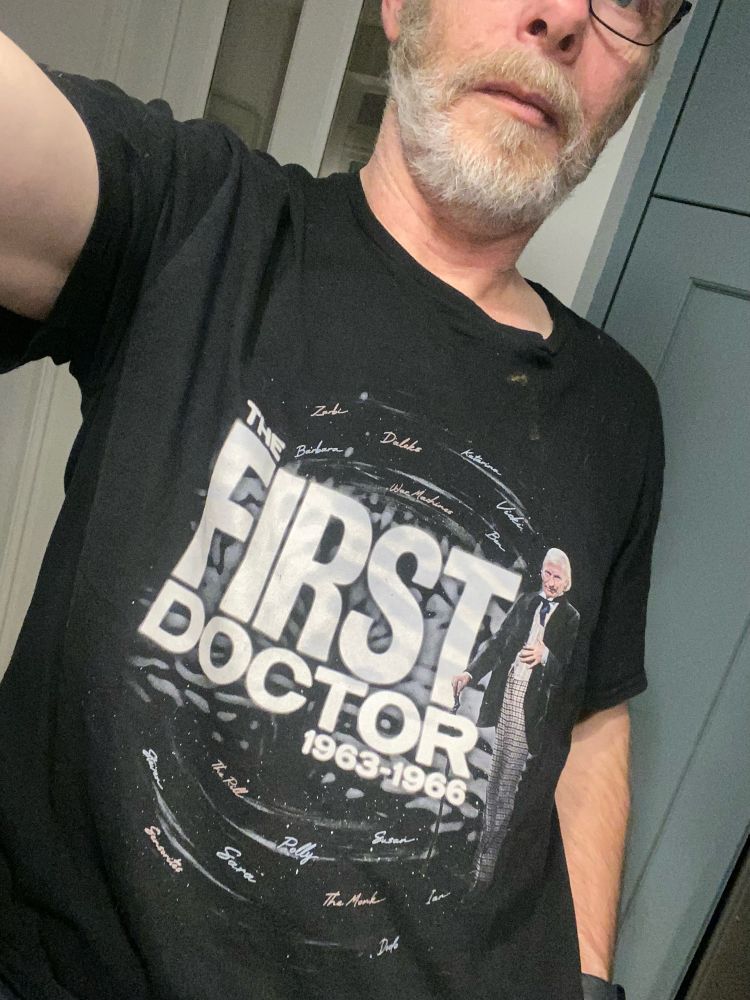 Picture of bearded man wearing a T-shirt with First Doctor written on it and a picture of William Hartnell in Dr Who costume