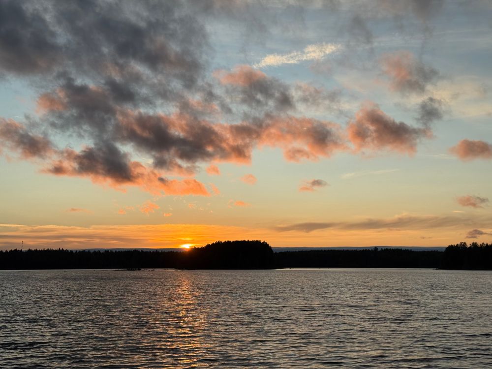 Aurinko laskemassa ja värjäämässä taivaan siniseksi, punaiseksi ja violetiksi.
