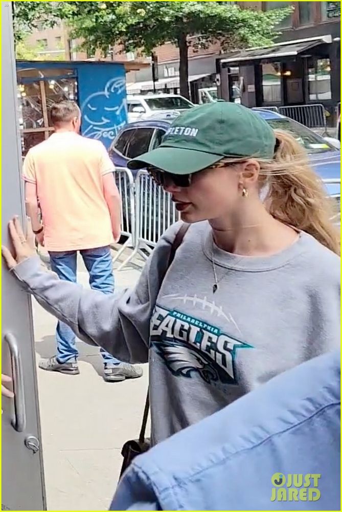 Taylor Swift wearing green baseball cap and gray eagle pullover sweater