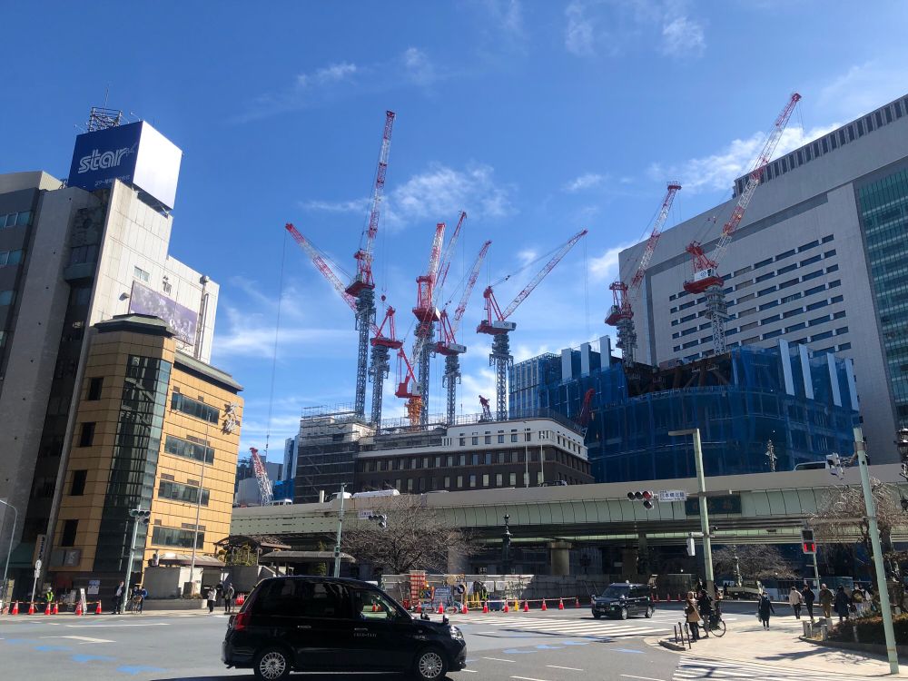 青空を背景にクレーンがたちならぶビル建設現場