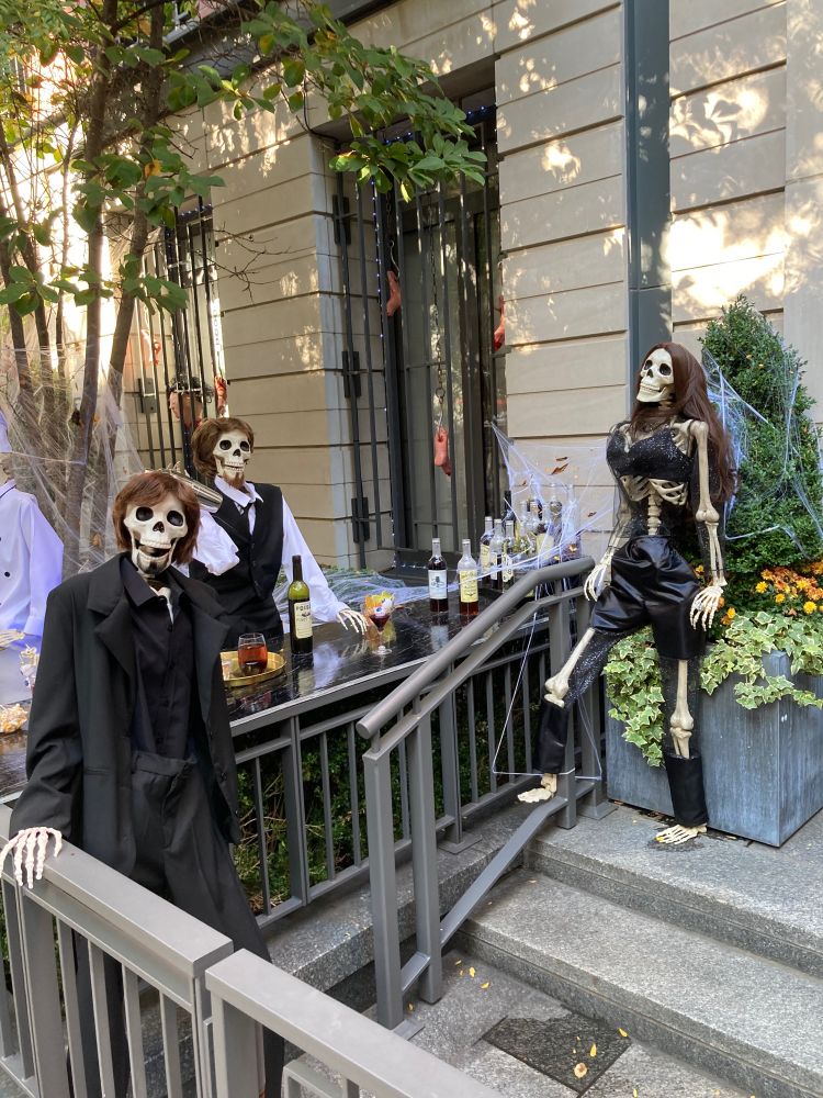 A display of Halloween effigies enjoying a drink in a bar. Skeletons in black attire, looking like real New Yorkers.