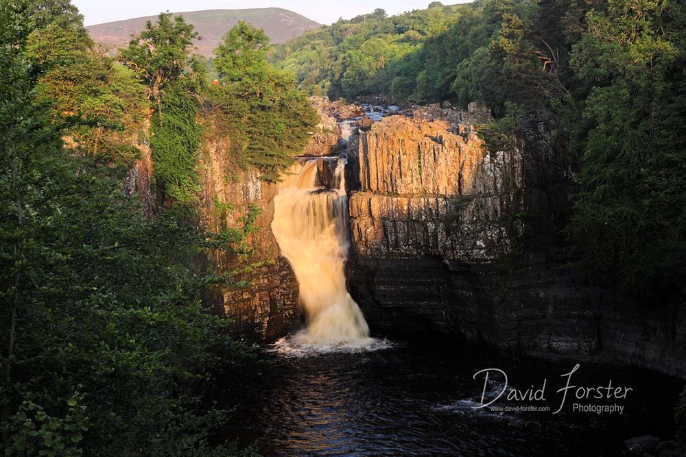The rising sun illuminates High Force waterfall with a golden light. 