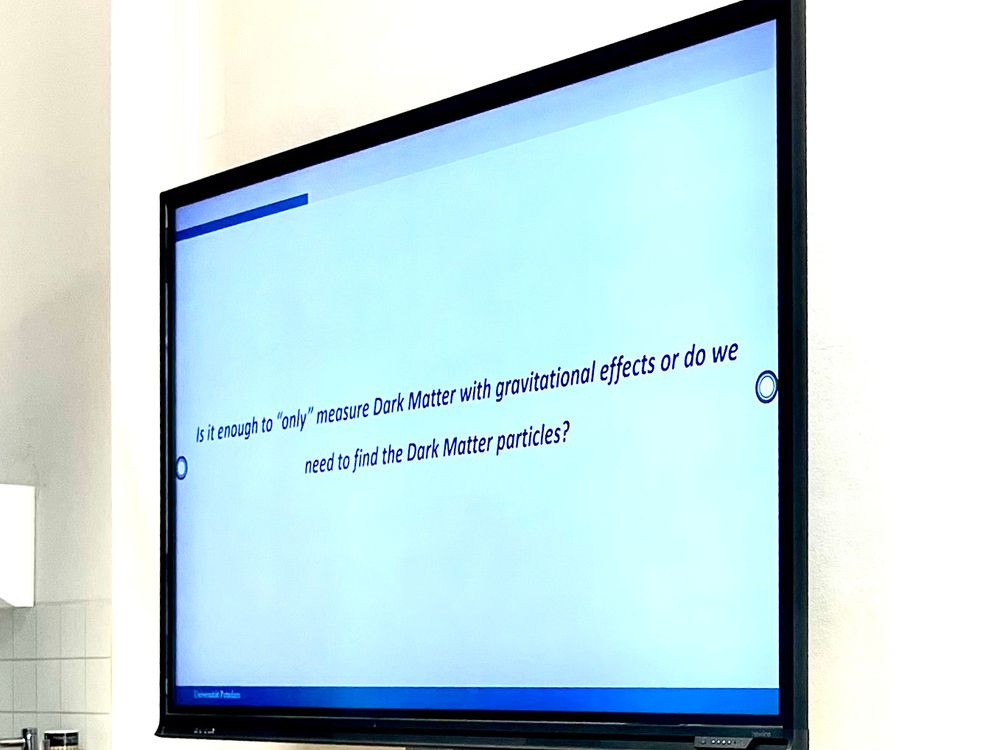 Screen showing a presentation slide reading “Is it enough to "only" measure Dark Matter with gravitational effects or do we need to find the Dark Matter particles?”