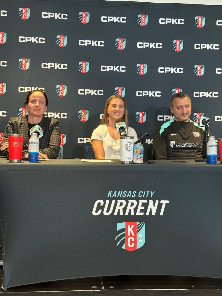 Kaitlin Carducci, Ally Sentnor and Vlatko Andonovski sitting at a table in front of a KC Current backdrop. 