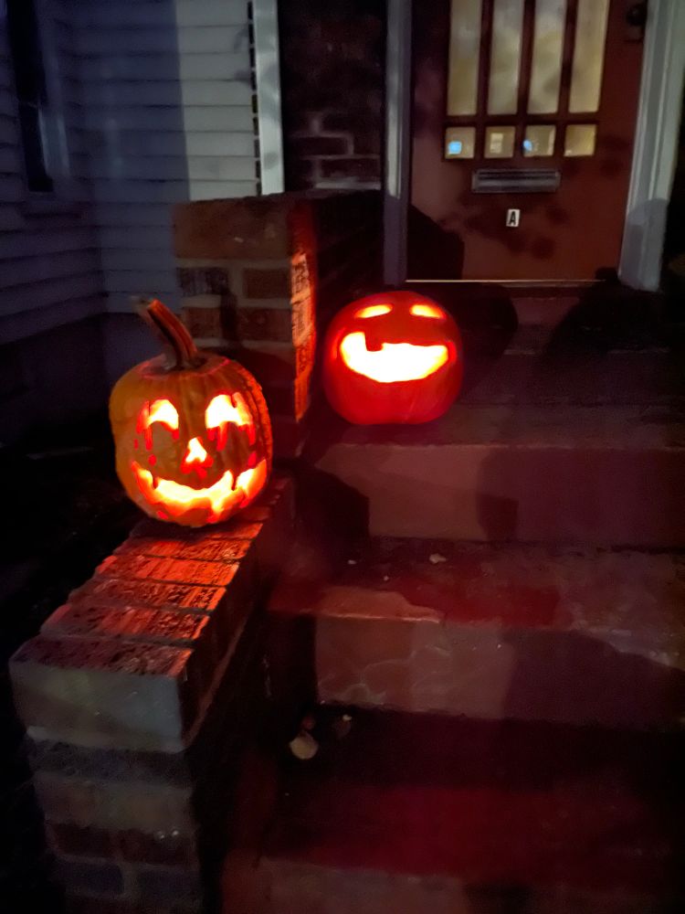 Two lit up pumpkins, one with a belting smiling face and the other with a big grin