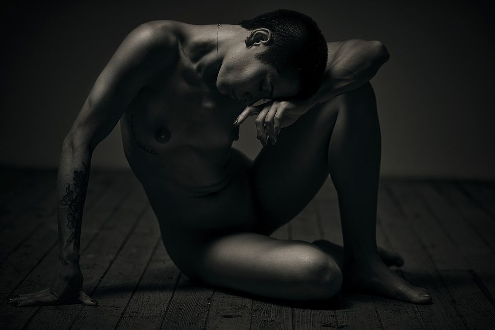 Black and white horizontal photo of model August Hayashi posed on studio floor.