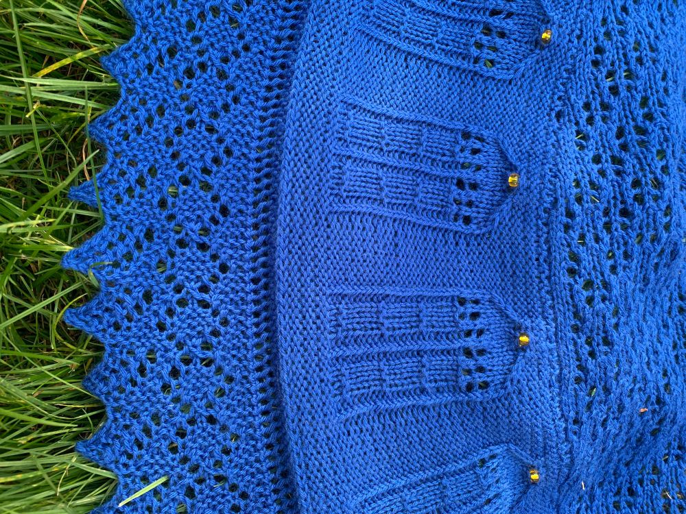 Blue crescent shaped shawl with a pattern of police boxes and lace edging. Yellow beads for the lights in the police boxes. The pattern is “Bigger on the inside” by Kate Atherley with a modified lace edge