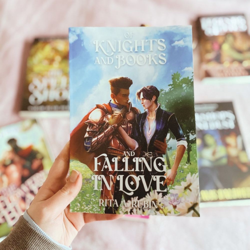 A photo of a white hand holding a copy of Of Knights and Books and Falling In Love by Rita A. Rubin
