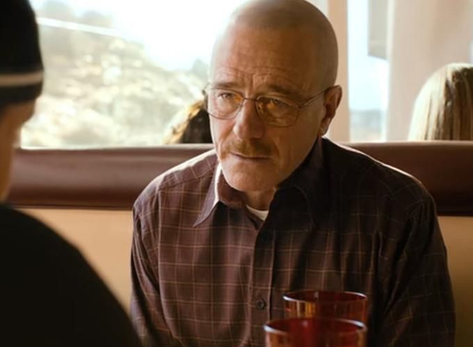 The character Walter White, portrayed by Bryan Cranston, from the acclaimed TV series Breaking Bad (2008), is sitting in a table booth at a Denny's restaurant. Walter is looking at his business associate, Jesse Pinkman, with an exhausted expression. 