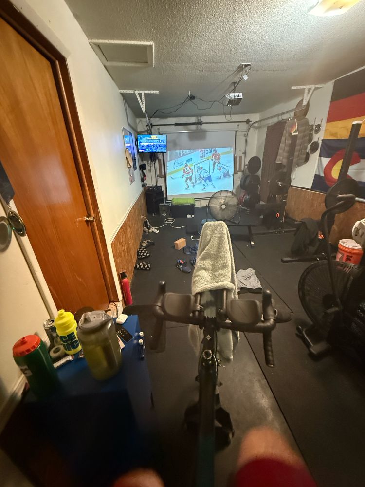 A home gym with a projector screen of the NHL and the cycling program Zwift on a second screen 