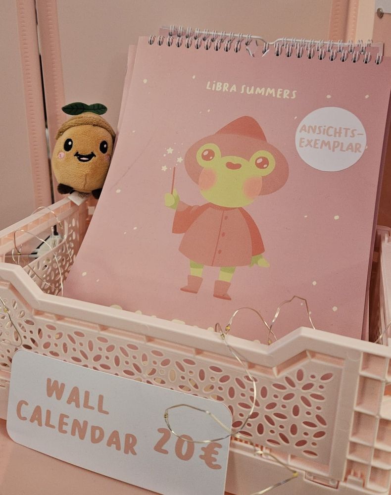 A photo of a wall calendar sitting in a pink crate. It has a wizard frog on the front