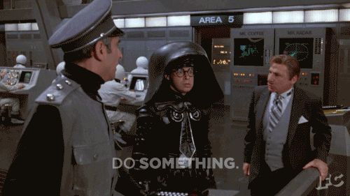 A screenshot of the main villains from the movie Spaceballs (a spoof of Star Wars) aboard their space vessel. They are panicking- the President in a grey three-piece suit, Dark Helmet in a black Vader-like helmet with a tie, and the Colonel Sandurz in a pilot's cap and grey uniform. Each is shouting to the other, "Do something!"