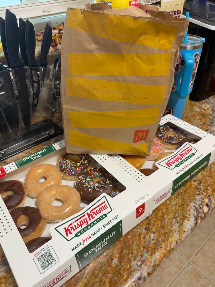 A picture of two cases of Krispy Kreme donuts and a bag of McDonald’s on top.