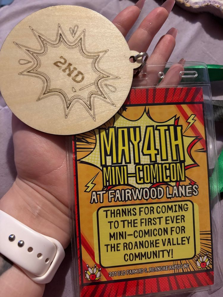 A convention badge reading “May 4th Mini-Comicon at Fairwood Lanes. Thanks for coming to the first ever Mini-Comicon for the Roanoke Valley Community”. Also a wooden 2nd place award sitting to the top of the badge.