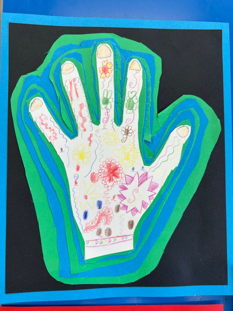 A photo of a cutout of a child’s had that has been decorated with colourful doodles backed onto green and blue cardboard.