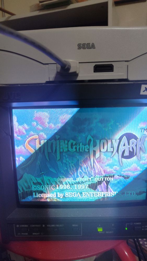 A SEGA Saturn on a red stool displaying Shining the Holy Ark on a small CRT