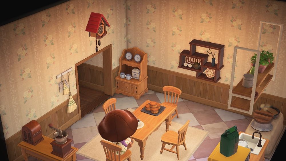 my kitchen in the game animal crossing new horizons. the furniture is all a light wood color, there's a table with a cup of coffee and come pastries on it and four chairs surrounding it and my character is sitting at the end chair facing away. a table behind her has a coffee grinder and an old radio. to her right along the wall showing is a yellow fridge with a green bag of coffee beans on top, a counter with a jar of cookies and a sink in front of a window with hanging shelves above it, then finally a stone stove that is burning with pots and pans hanging above it. the walls are  an off white with white roses on it, the floor is a white and grey checkered tile and there is an off white rug under the table. in the far corner is a china cabinet and some shelving on the wall next to it and on the otherside it the entryway. above the entrance is a coocoo clock and next to it is a broom hanging on the wall
