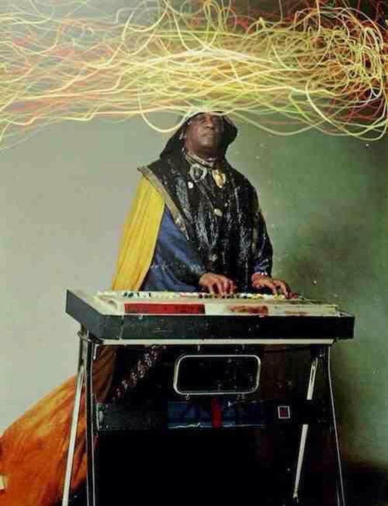 Sun Ra at a keyboard with a cape with a mass of electric squiggles in a cloud emanating from his head 